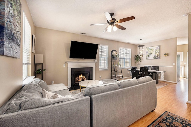 living area featuring visible vents, baseboards, light wood-type flooring, a warm lit fireplace, and a ceiling fan