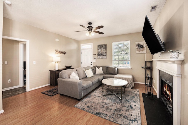 living room with visible vents, a fireplace with flush hearth, a textured ceiling, wood finished floors, and ceiling fan