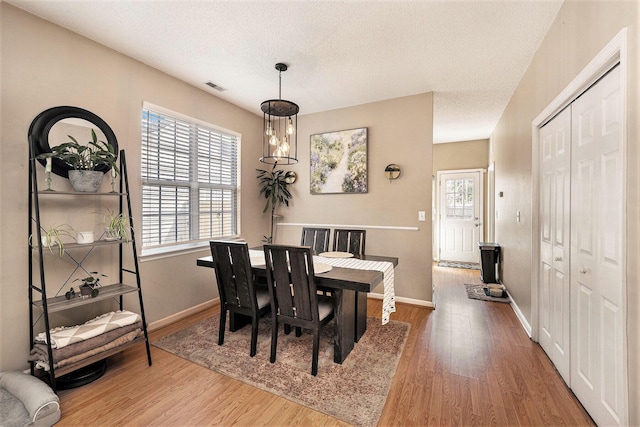 dining room featuring baseboards, wood finished floors, visible vents, and a textured ceiling