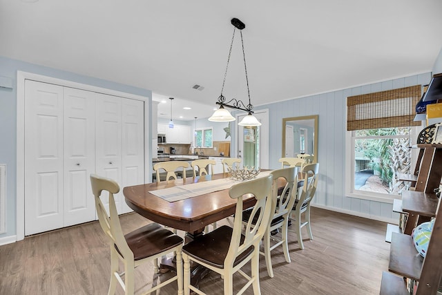 dining space featuring light wood-type flooring, wooden walls, and plenty of natural light