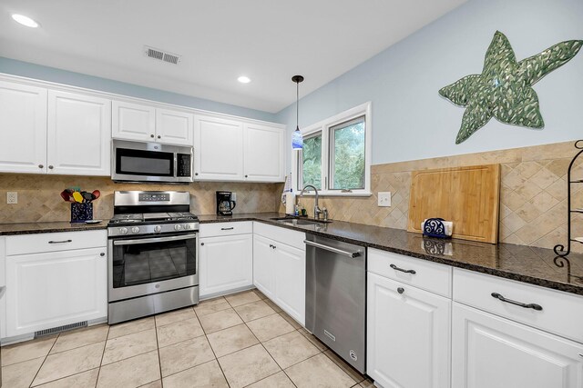 kitchen with stainless steel appliances, white cabinetry, sink, dark stone counters, and pendant lighting