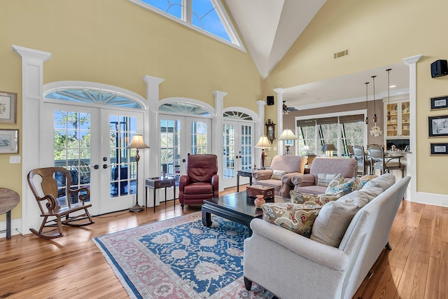 living room with french doors, a towering ceiling, and light hardwood / wood-style floors