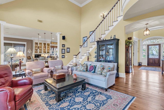 living room featuring a towering ceiling, ornamental molding, wood-type flooring, and ornate columns