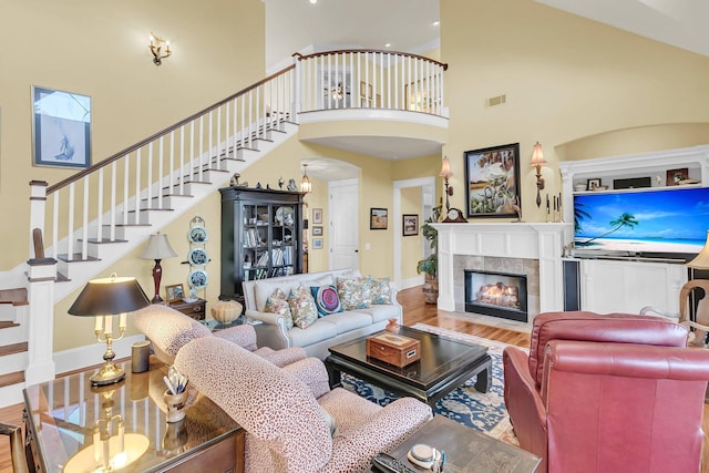 living room featuring hardwood / wood-style flooring, a towering ceiling, and a tiled fireplace