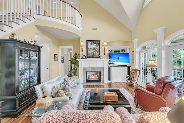 living room with hardwood / wood-style flooring, high vaulted ceiling, a tiled fireplace, french doors, and ornate columns