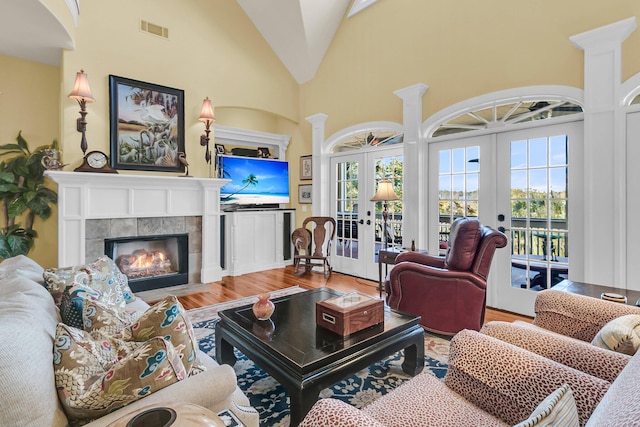 living room with french doors, high vaulted ceiling, hardwood / wood-style floors, a fireplace, and decorative columns