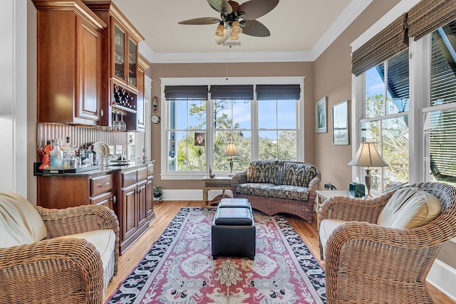 interior space with ornamental molding, indoor wet bar, ceiling fan, and light hardwood / wood-style flooring