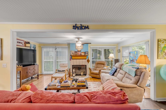 living room featuring ornamental molding, light hardwood / wood-style floors, a tile fireplace, and ceiling fan