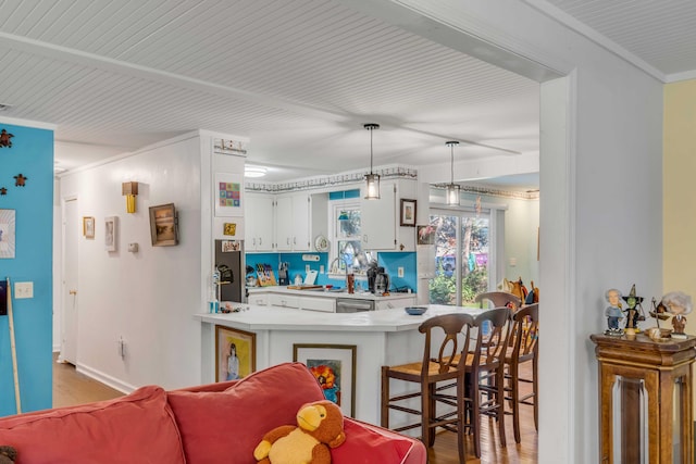 kitchen featuring pendant lighting, light hardwood / wood-style flooring, white cabinetry, ornamental molding, and kitchen peninsula