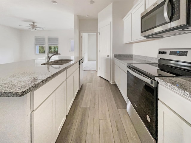 kitchen with light stone countertops, light wood-type flooring, white cabinets, stainless steel appliances, and a sink