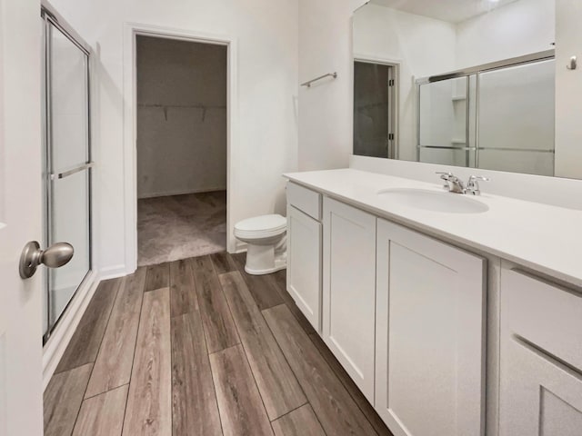 bathroom featuring a shower stall, a walk in closet, toilet, wood finished floors, and vanity