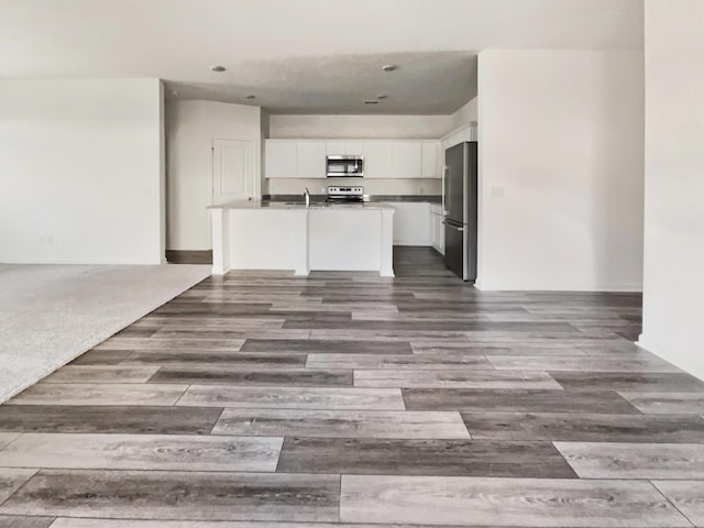 kitchen featuring wood finished floors, a sink, stainless steel appliances, white cabinets, and open floor plan