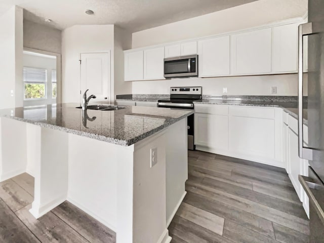 kitchen with dark wood-type flooring, a sink, white cabinetry, dark stone counters, and appliances with stainless steel finishes