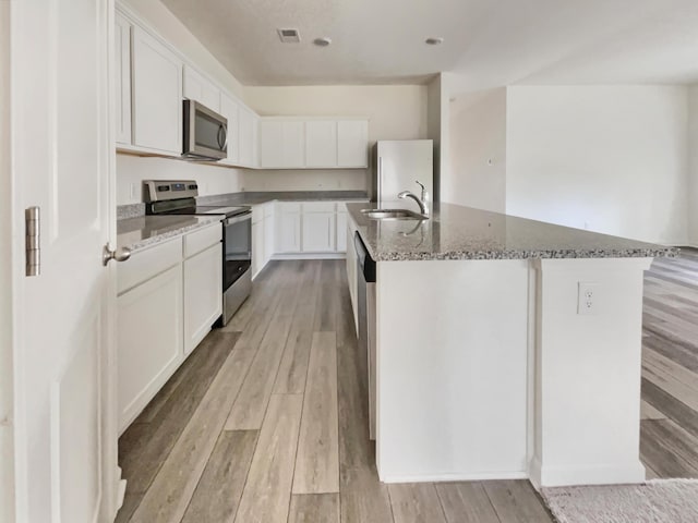 kitchen with visible vents, a sink, dark stone counters, appliances with stainless steel finishes, and light wood finished floors