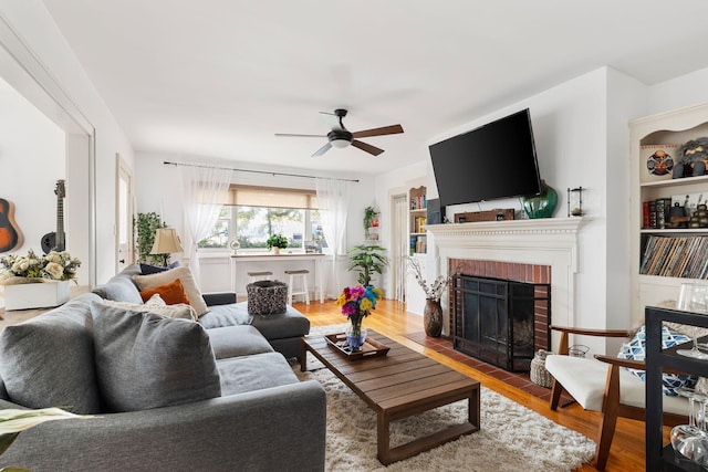 living room with hardwood / wood-style floors, ceiling fan, and a brick fireplace