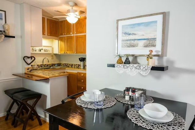 kitchen with a sink, a kitchen breakfast bar, a peninsula, and a ceiling fan