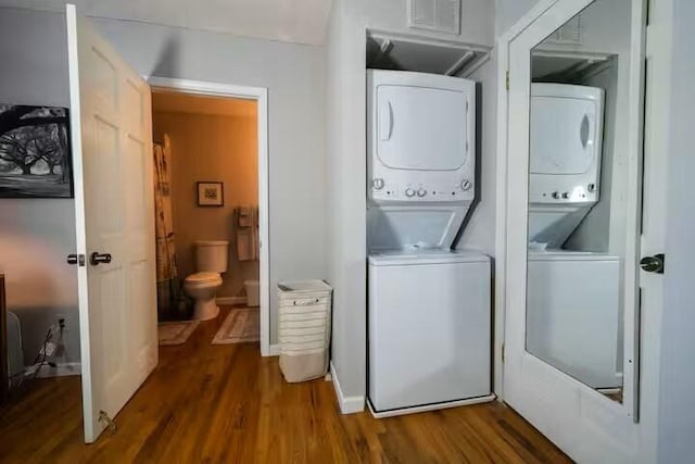 laundry area with laundry area, wood finished floors, baseboards, and stacked washing maching and dryer