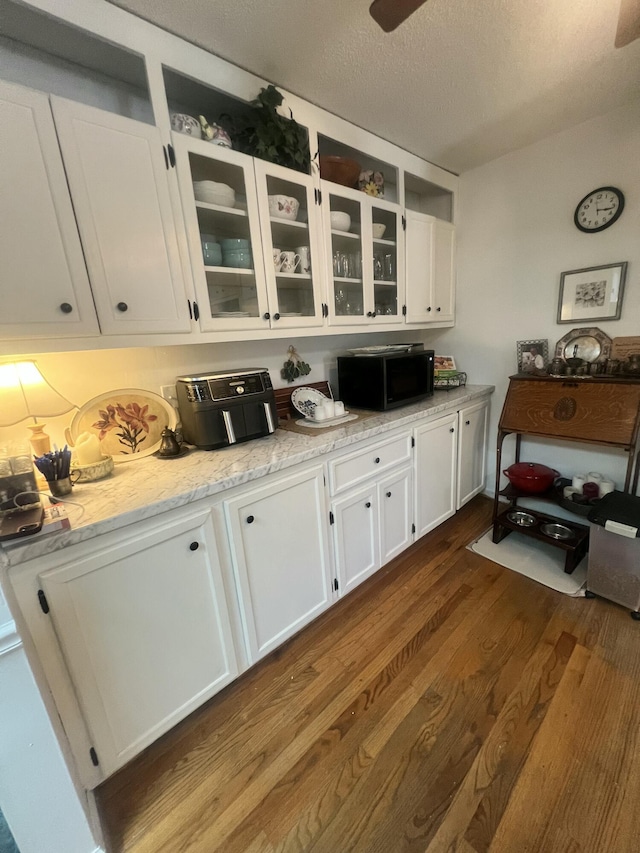 kitchen with glass insert cabinets, dark wood finished floors, black microwave, and white cabinetry