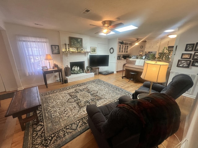 living room featuring visible vents, a fireplace, light wood-style floors, and a ceiling fan