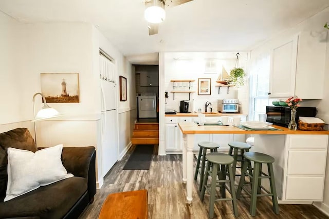 kitchen featuring white cabinetry, freestanding refrigerator, black microwave, washer / dryer, and dark wood-style flooring