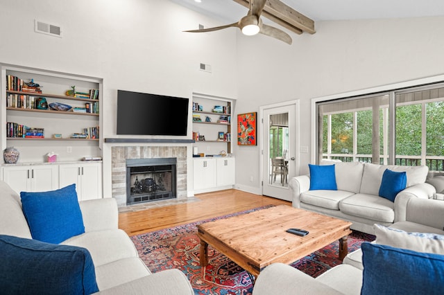 living room with ceiling fan, beam ceiling, hardwood / wood-style flooring, a fireplace, and a high ceiling