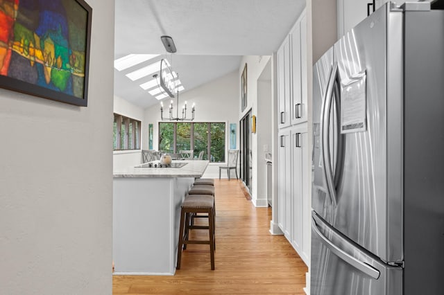 kitchen featuring hanging light fixtures, stainless steel fridge, a chandelier, a breakfast bar area, and white cabinets