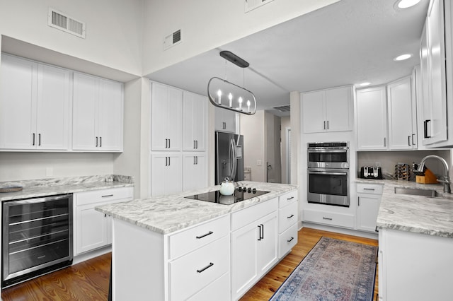 kitchen with white cabinets, hanging light fixtures, sink, appliances with stainless steel finishes, and beverage cooler