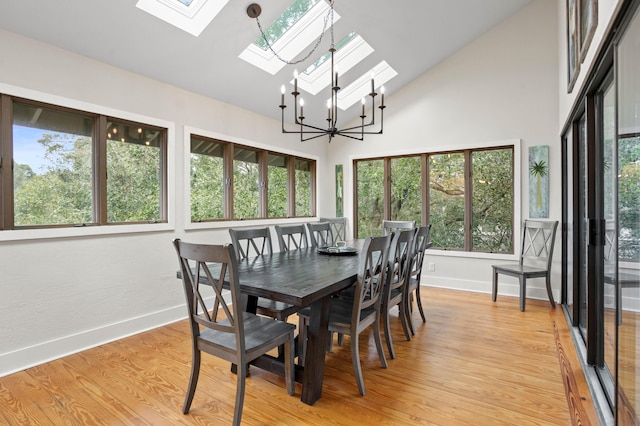 dining room featuring a skylight, high vaulted ceiling, a chandelier, and light wood-type flooring