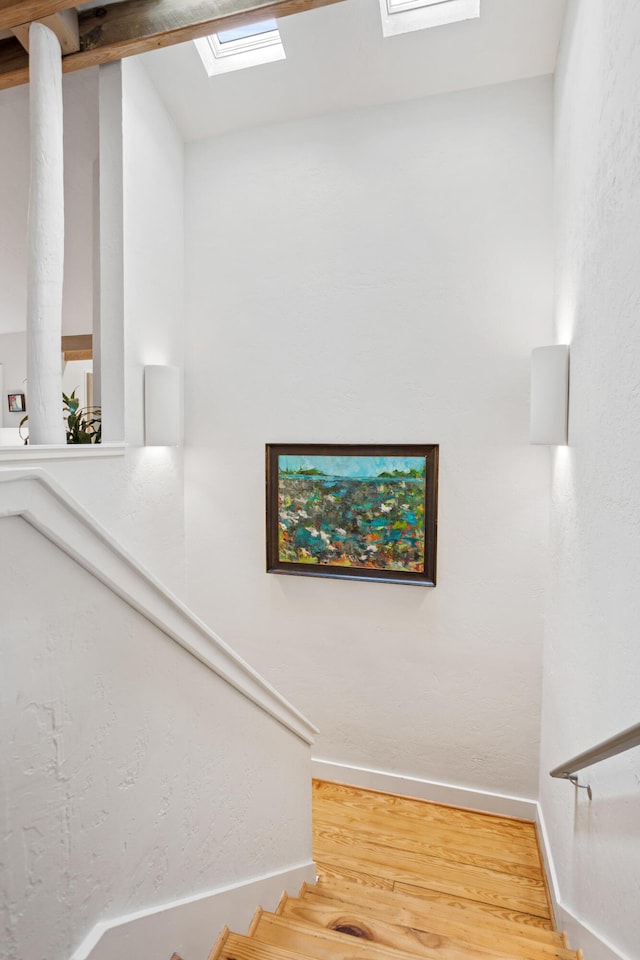 stairs with wood-type flooring and lofted ceiling with skylight