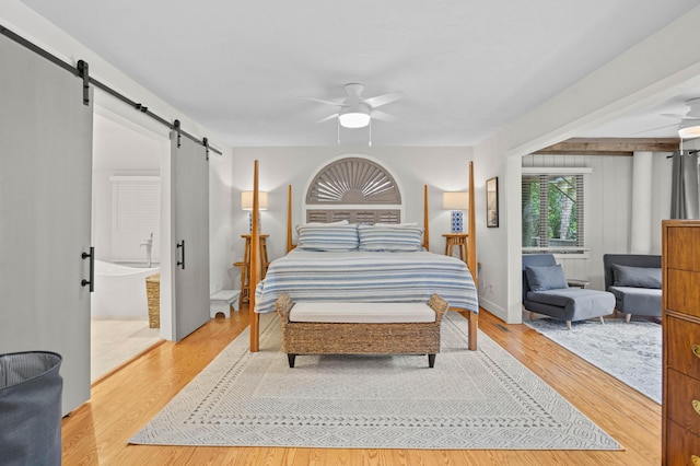 bedroom featuring ensuite bath, ceiling fan, wood-type flooring, and a barn door