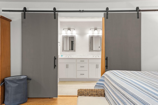 bedroom featuring a barn door, light hardwood / wood-style floors, ensuite bath, and sink