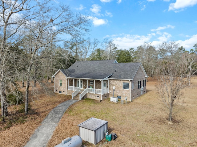 view of front of home with covered porch, brick siding, a shingled roof, crawl space, and a front yard