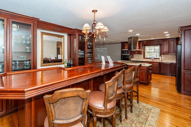 bar featuring pendant lighting, a textured ceiling, island exhaust hood, light hardwood / wood-style floors, and stainless steel oven