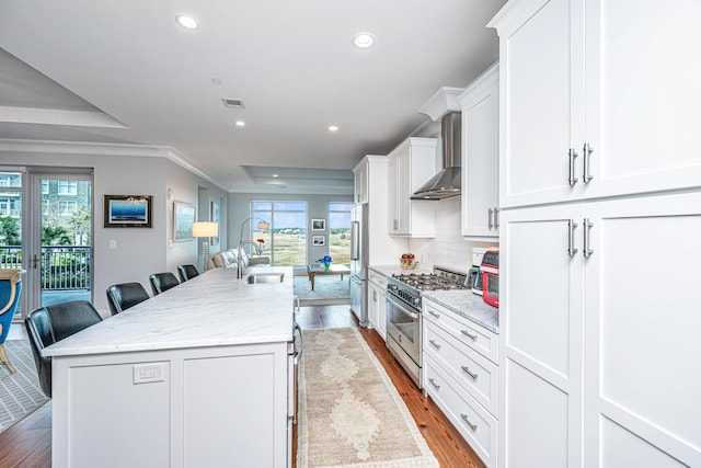 kitchen featuring wall chimney exhaust hood, a breakfast bar, high end appliances, a kitchen island with sink, and white cabinets