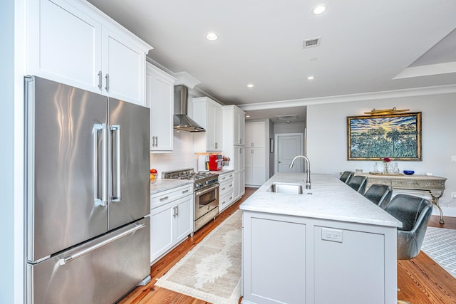 kitchen with white cabinets, premium appliances, light hardwood / wood-style flooring, and wall chimney exhaust hood