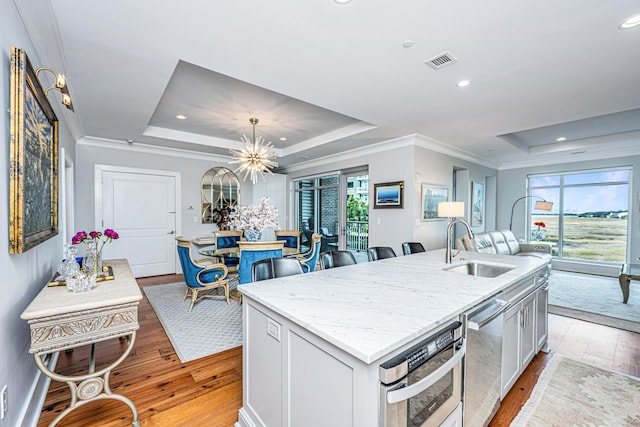 kitchen featuring an inviting chandelier, light wood-type flooring, a kitchen island with sink, and a tray ceiling