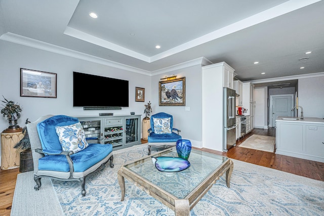 living room featuring wood-type flooring, a raised ceiling, and crown molding