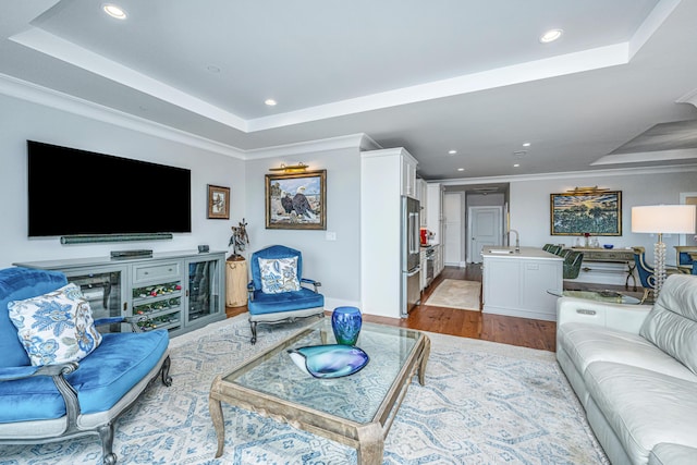 living room with a tray ceiling, sink, ornamental molding, and light wood-type flooring