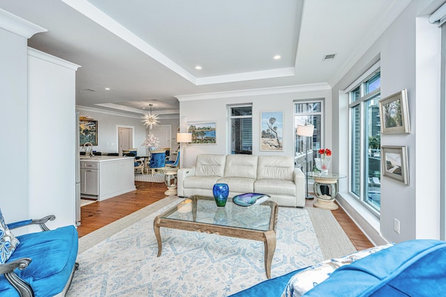 living room with a notable chandelier, ornamental molding, light hardwood / wood-style flooring, and a tray ceiling