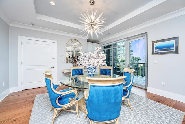 dining space with a raised ceiling, light hardwood / wood-style flooring, ornamental molding, and a notable chandelier