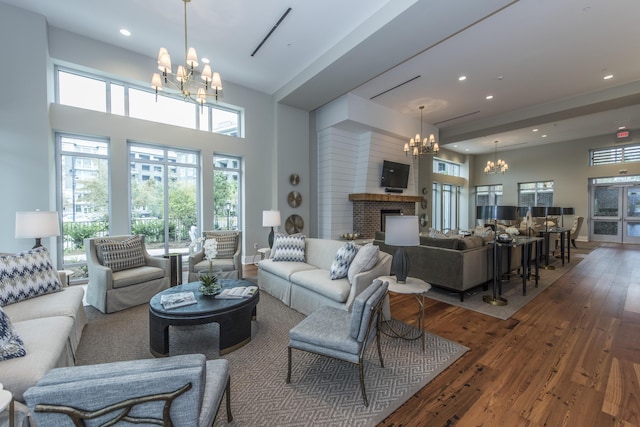 living room featuring a high ceiling, an inviting chandelier, a brick fireplace, and dark wood-type flooring