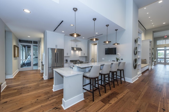 kitchen featuring light stone countertops, high end fridge, a breakfast bar, white cabinets, and hanging light fixtures