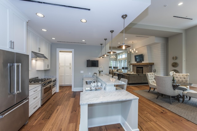 kitchen with white cabinetry, hanging light fixtures, a brick fireplace, premium appliances, and light stone counters