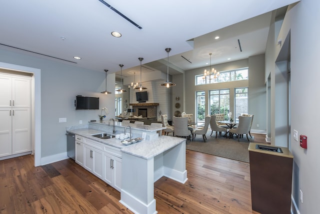 kitchen featuring a breakfast bar, white cabinets, sink, a brick fireplace, and light stone counters