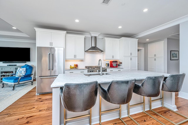 kitchen with white cabinets, wall chimney range hood, a kitchen island with sink, and high quality fridge