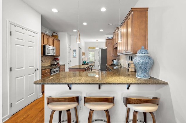 kitchen featuring stainless steel appliances, dark stone counters, decorative backsplash, sink, and kitchen peninsula