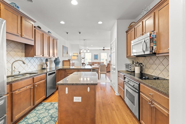 kitchen featuring a kitchen island, sink, hanging light fixtures, appliances with stainless steel finishes, and dark stone counters