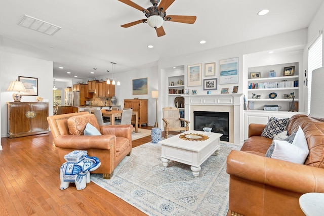 living room with ceiling fan, built in features, and light hardwood / wood-style flooring