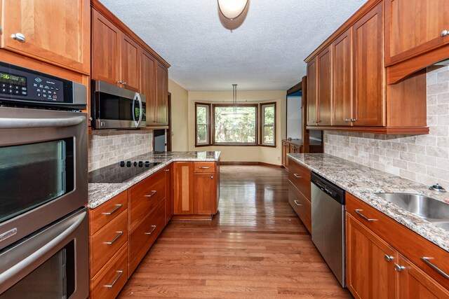 kitchen featuring light wood-type flooring, appliances with stainless steel finishes, hanging light fixtures, and decorative backsplash