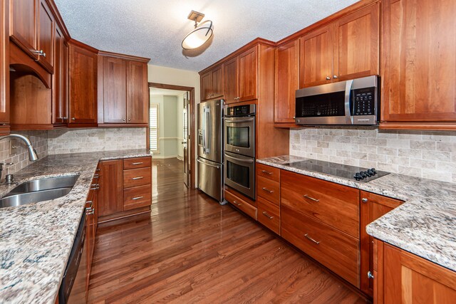 kitchen featuring backsplash, appliances with stainless steel finishes, light stone countertops, sink, and dark wood-type flooring